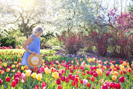 Une femme sourit et marche dans un jardin fleuri, son chapeau de paille à la main